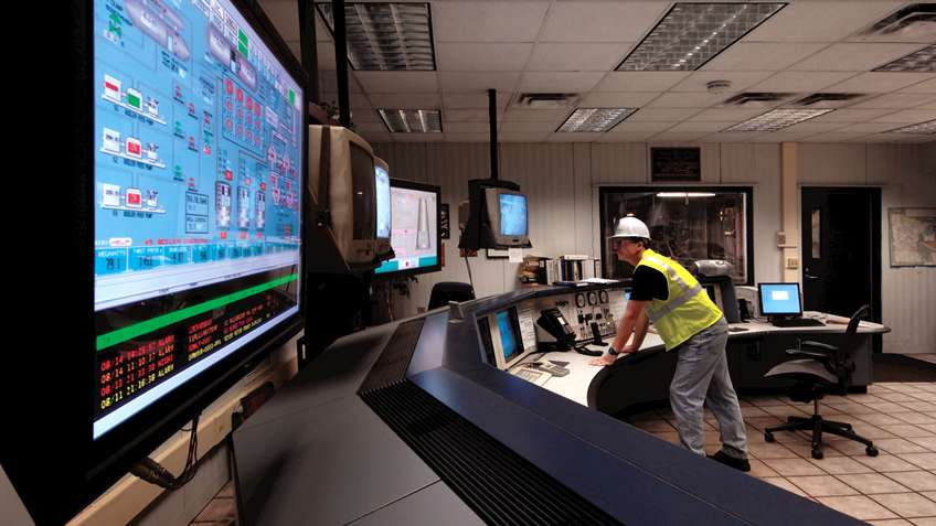 Operator at a control room console monitoring process graphics and alarm data on a large SCADA display