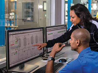 Two workers look at a computer screen on a production line.