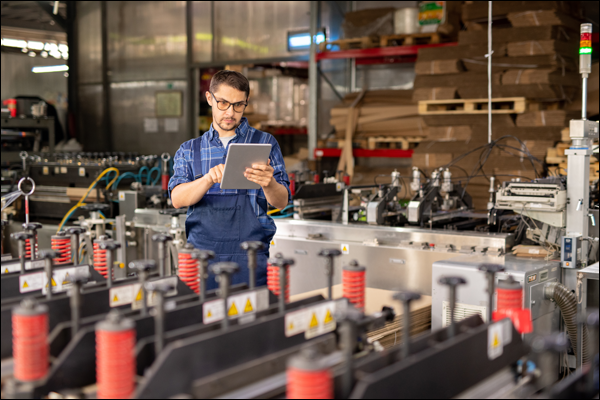 Technician reviewing machine data on a tablet beside a production line in a packaging facility