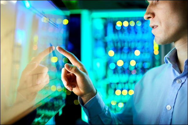 Man interacting with a glowing touchscreen interface in front of blurred network equipment racks