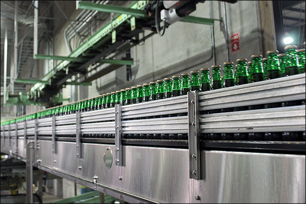 Beverage bottling conveyor line with stainless guide rails and overhead transfer conveyors