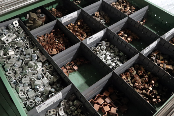 Divided storeroom bin drawer of copper and galvanized clamps and fittings with barcoded bin labels