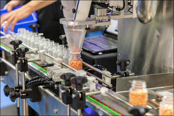 Automated bottle filling line dispensing capsules into containers on a conveyor with operator controls