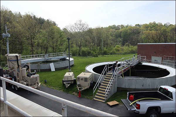 Wastewater treatment plant with circular clarifier tanks, portable pumping equipment, and crews working on site