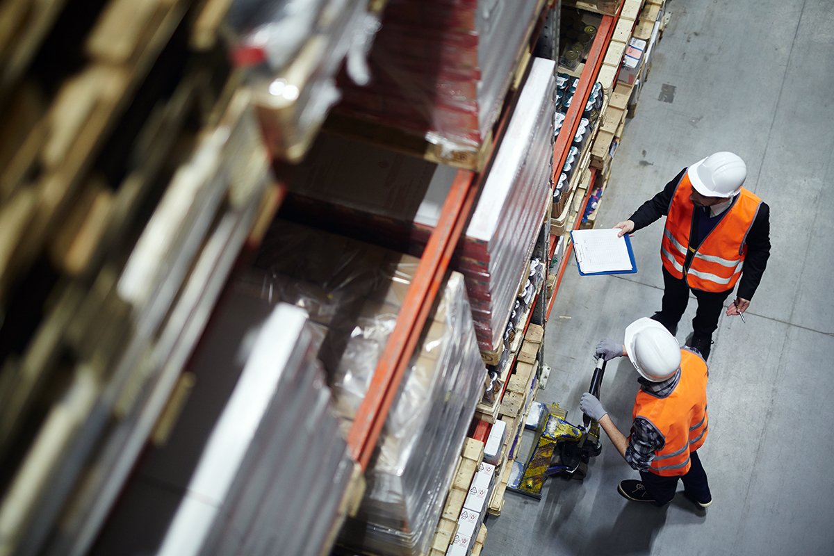 Warehouse staff with a clipboard and pallet jack checking stock levels in a racked storage aisle