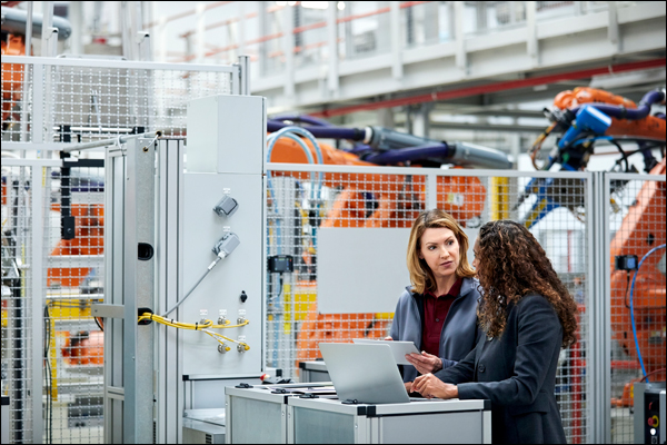 Two engineers reviewing equipment data on a laptop beside a control panel on a robotic automation line