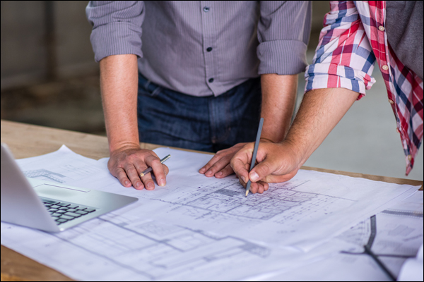 Two people marking up electrical construction drawings on a worktable during a project planning session