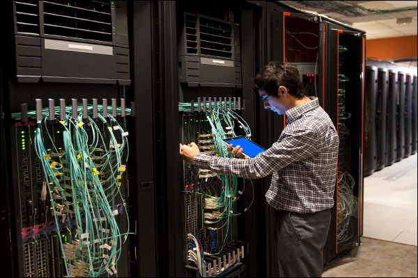 Technician auditing structured cabling and patch panel connections in a data center rack row